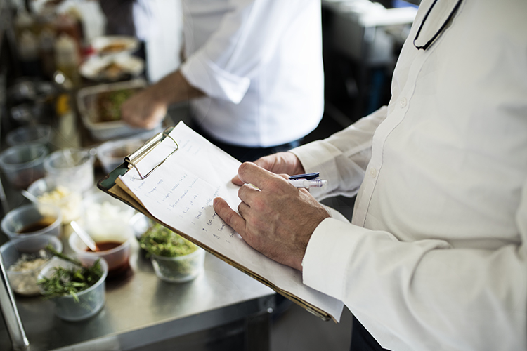 A food manager inspecting kitchen stations with a checklist
